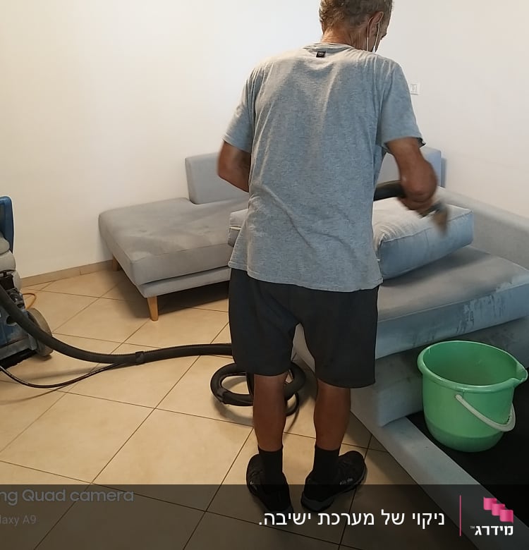 אדם מנקה ספה עם שואב אבק ודלי ירוק